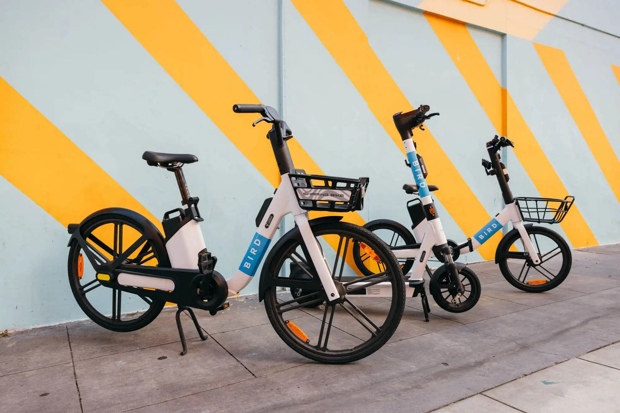 Bird e-bikes parked in front of a colourful yellow and teal mural